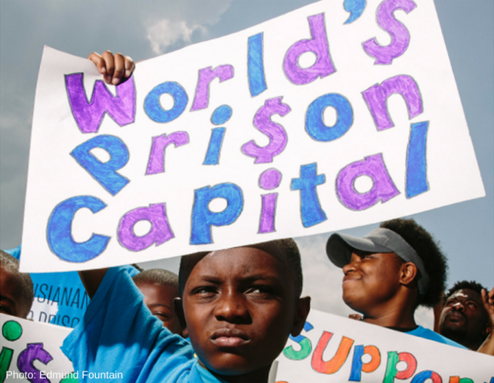 Photo of a young Black boy holding up a sign that reads "World's Prison Capital"