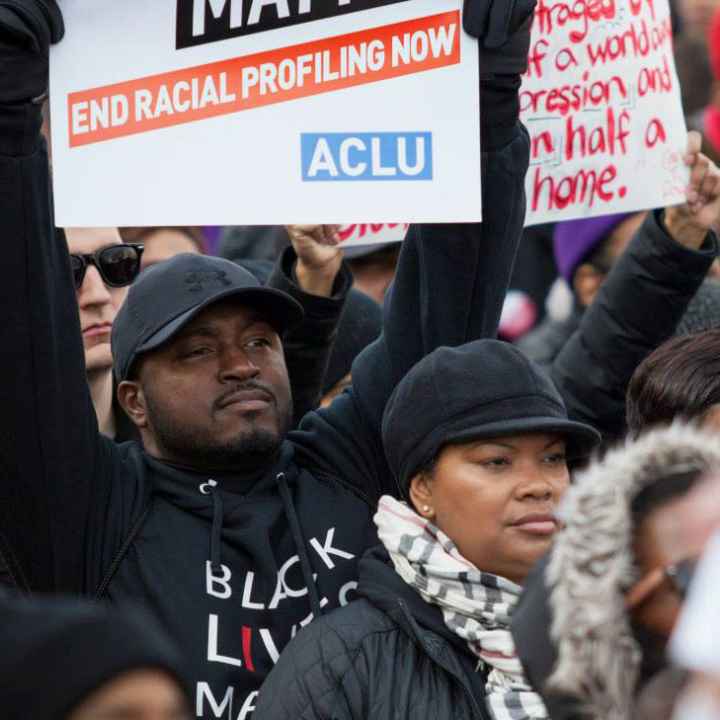 Black man holding a sign that reads "end racial profiling now"